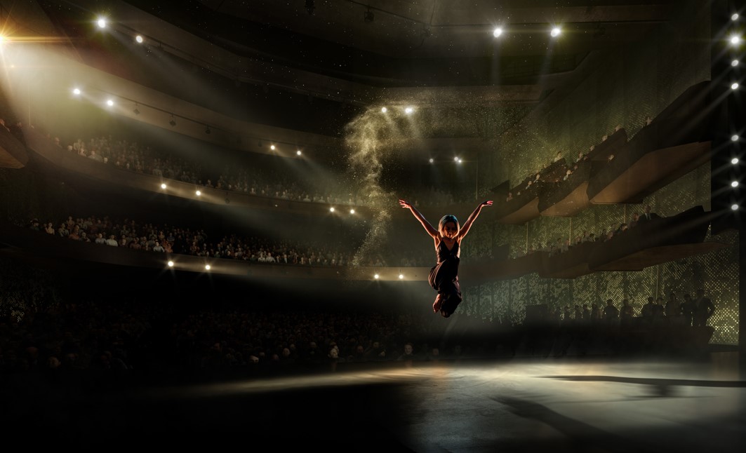 The image shows a performer on stage with a dark auditorium showing glimmers of the 2000 people that can fit in the venue