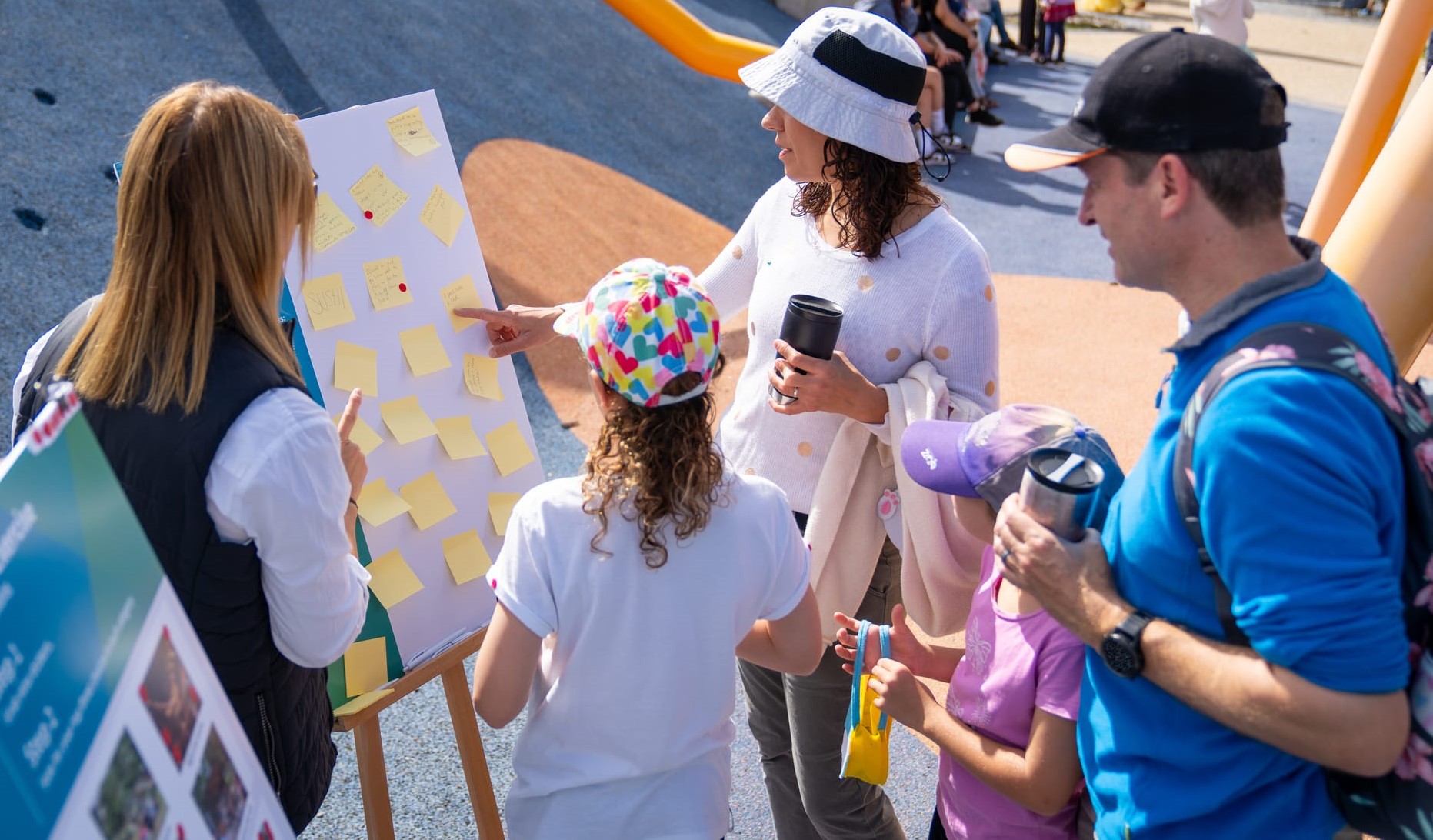 A family standing in front of an activity board adding their sticky notes with comments.